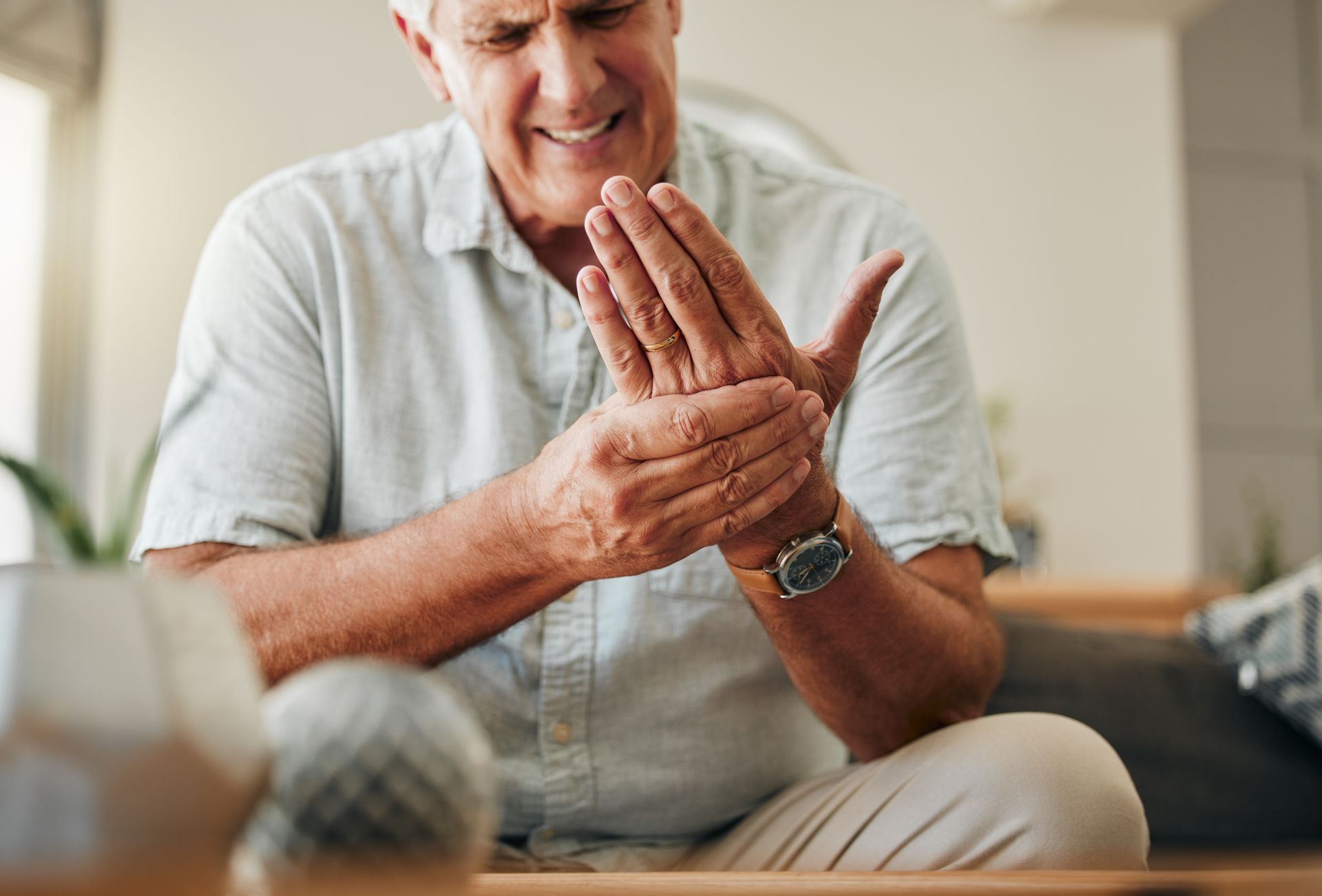 An individual in a light-colored shirt sits inside, holding their hand in discomfort with an expression of pain.