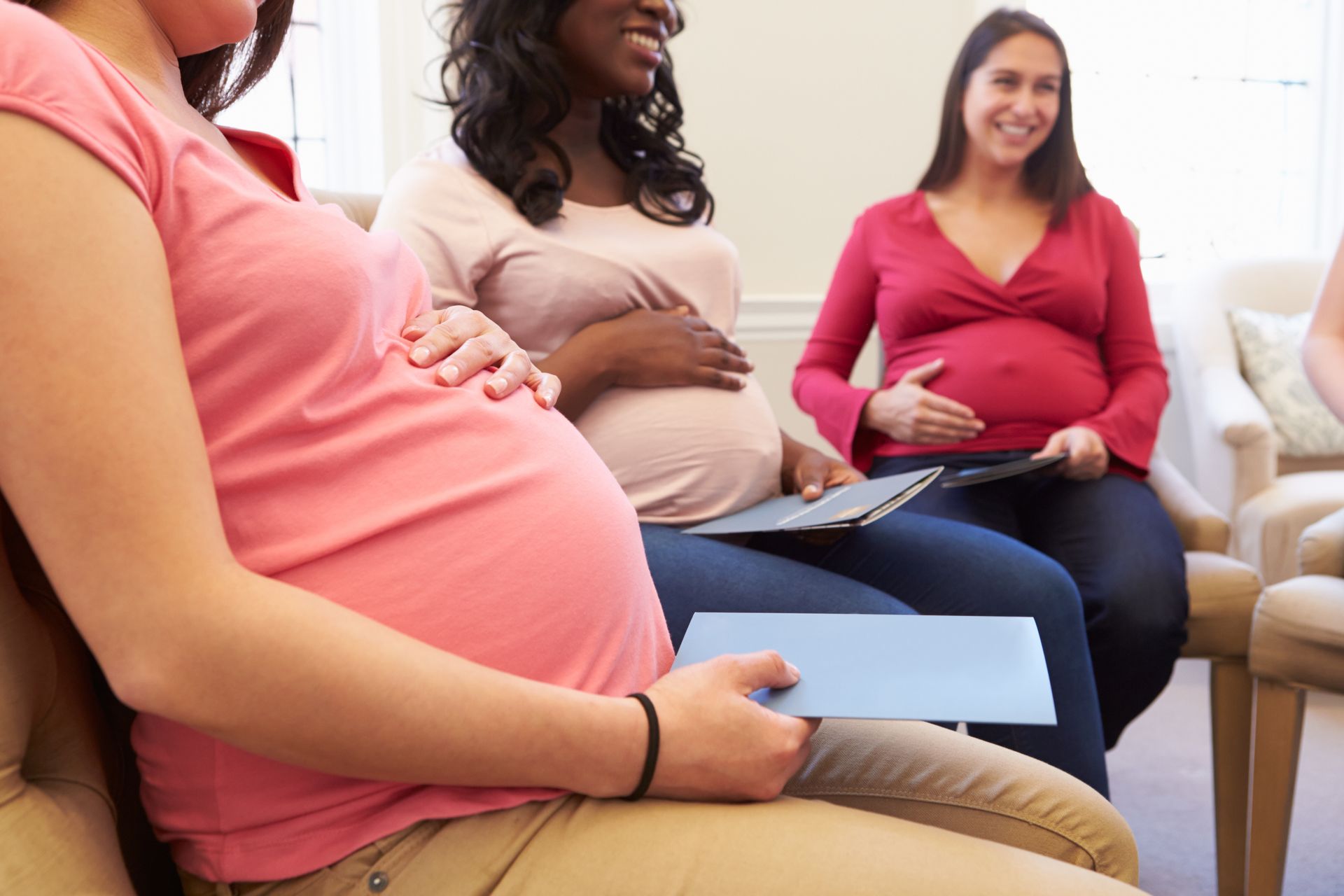 Three expectant individuals sit in a circle holding documents during a group meeting.