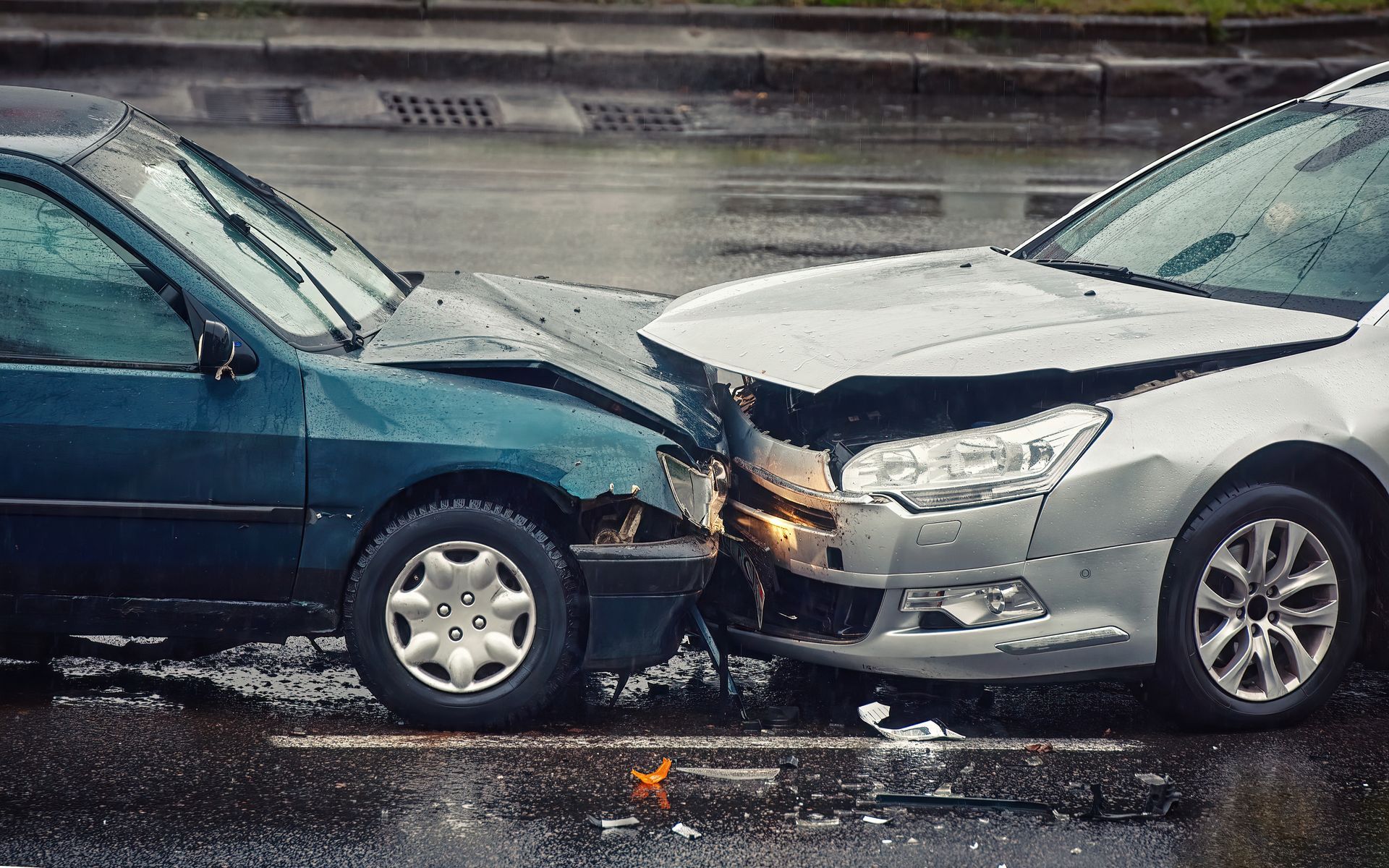 A silver car and a dark green car are shown after colliding head-on on a wet road.