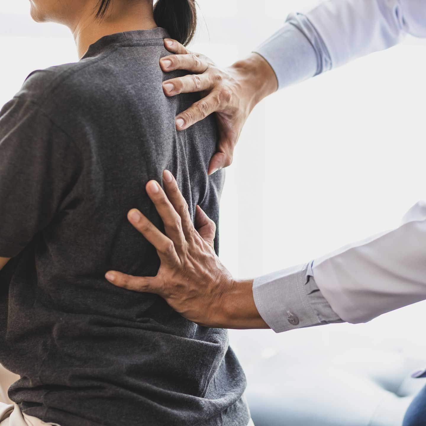 Person's back being examined by a doctor. Doctor's hands on back; indoors. A healthcare professional performs a manual physical examination of a patient's back.