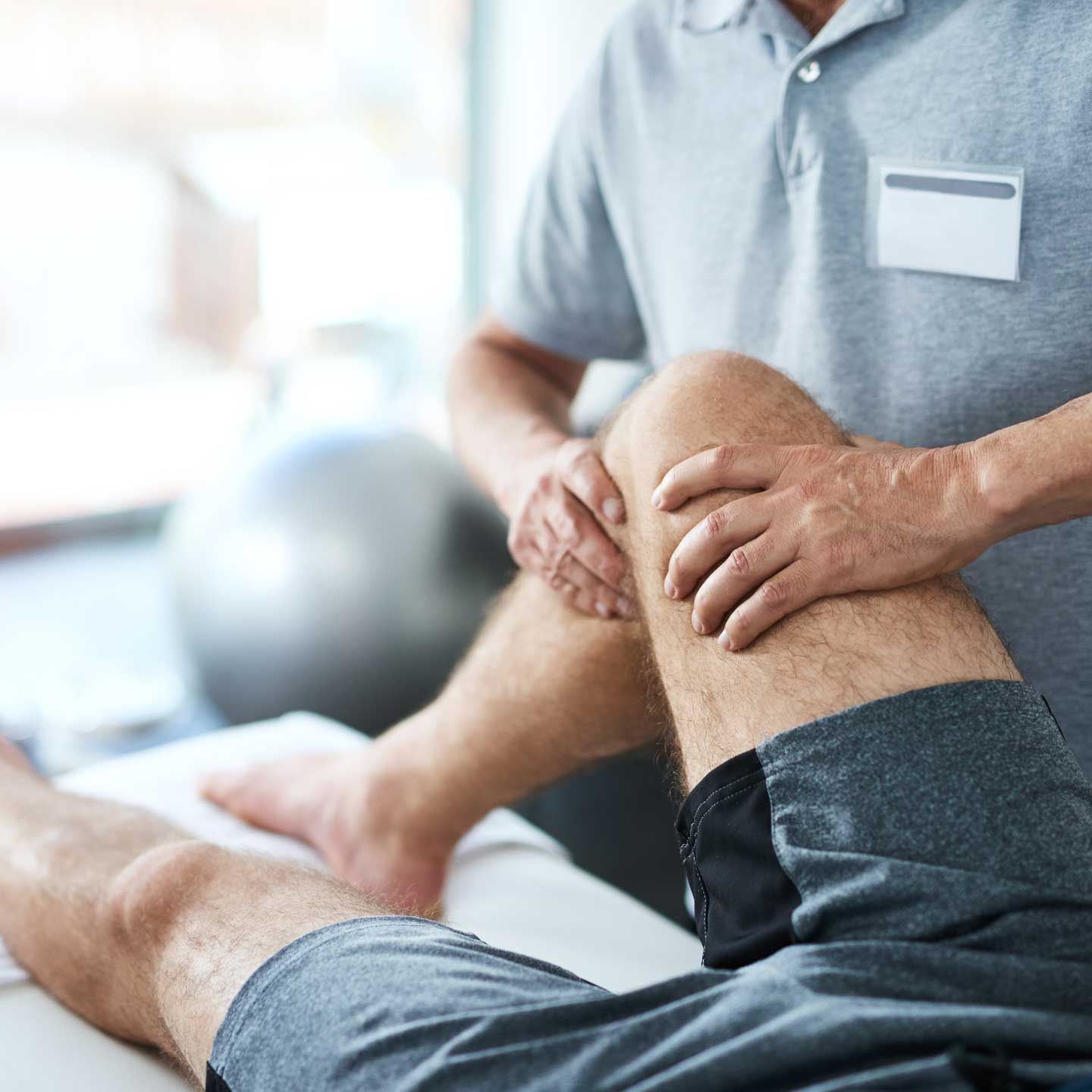 Physical therapist examining patient's knee in a clinic setting. A healthcare professional examines a patient's knee during a physical therapy session.