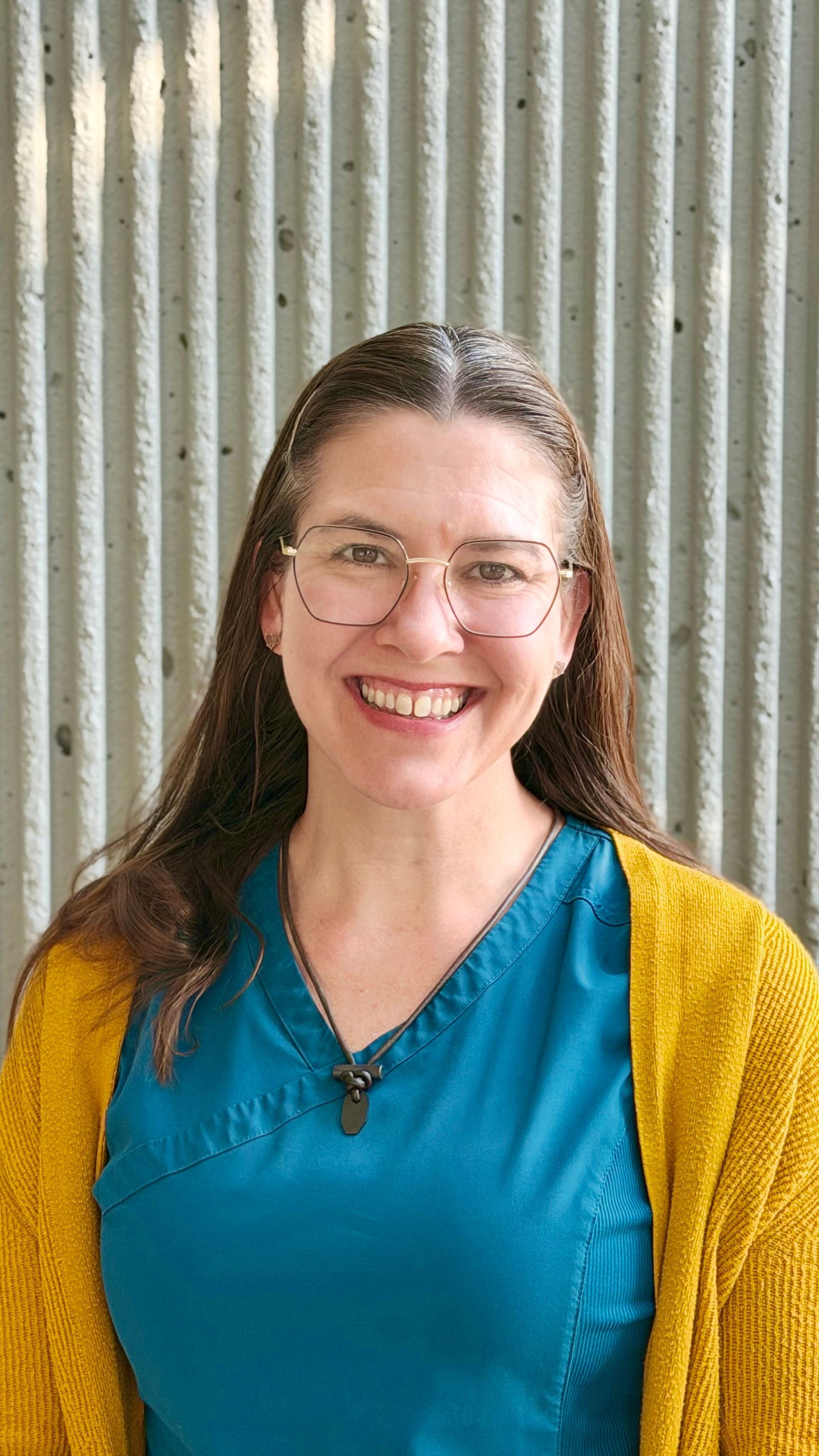 Woman with short hair smiles in a navy top in front of a textured, light-yellow wall.
