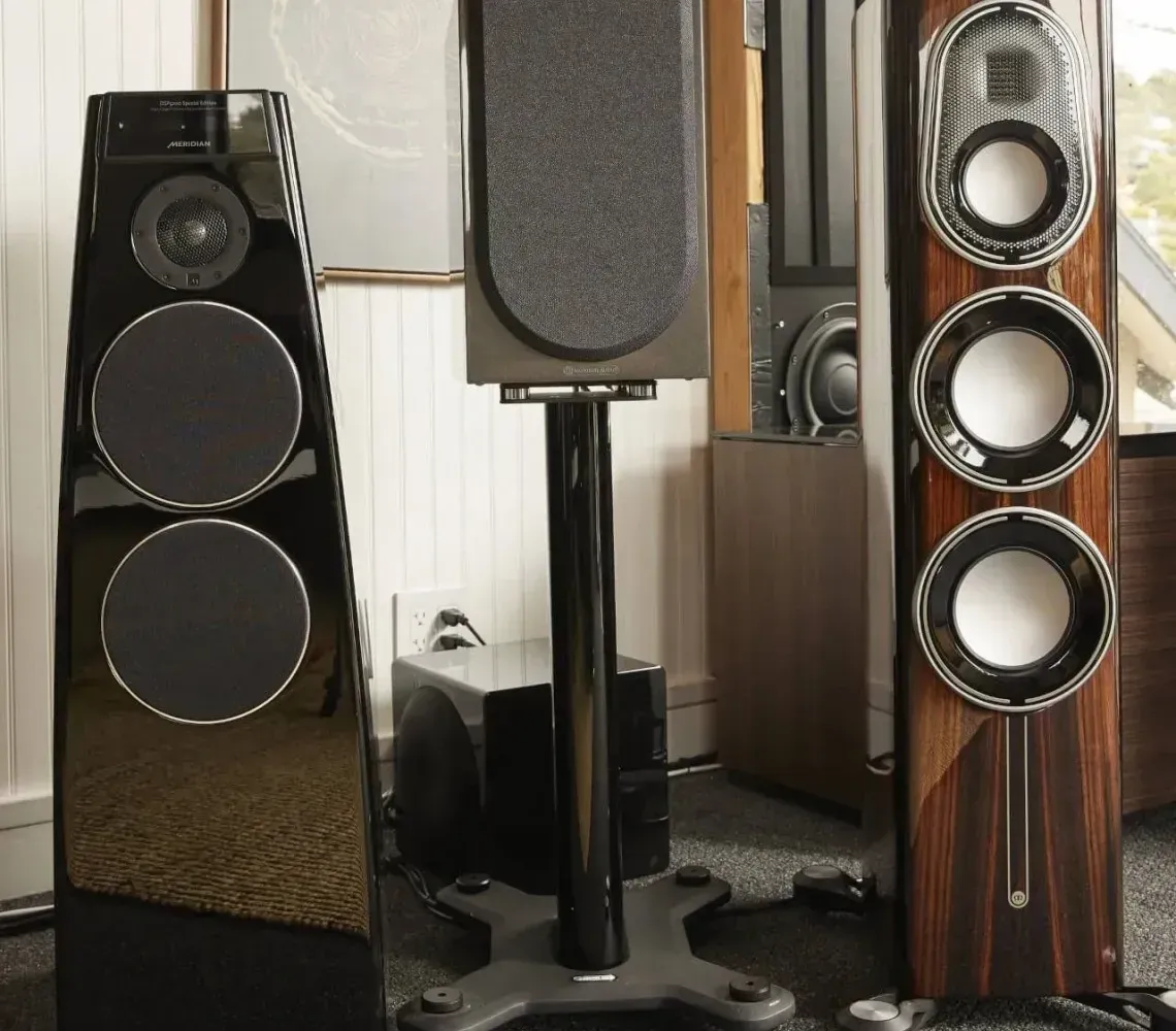 Three large floorstanding speakers in a room, including black and wood-grain models