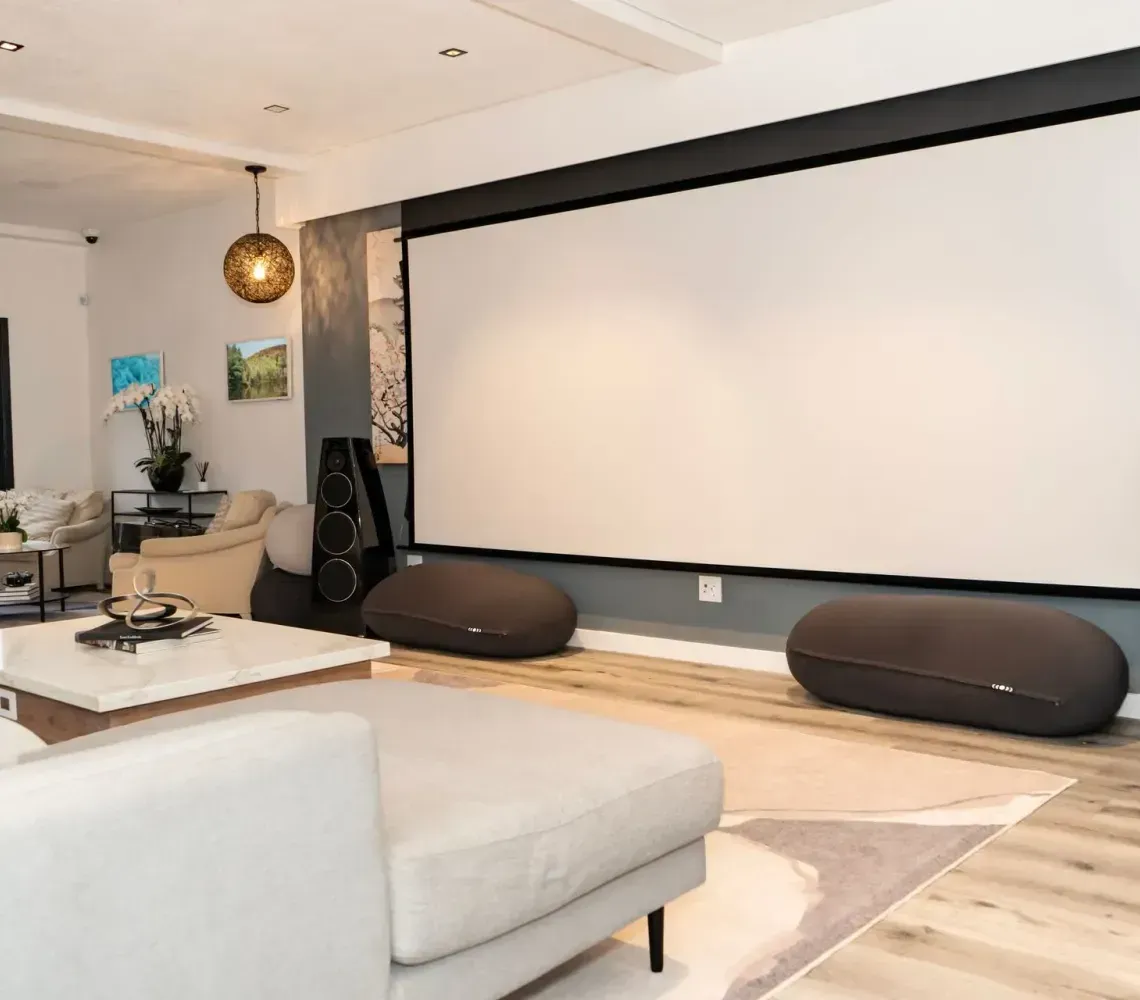 Modern home theater with a large projector screen, black speakers, and a light gray sectional sofa.