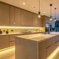 Modern minimalist kitchen with warm under-cabinet and island lighting, beige cabinets, and a long central island