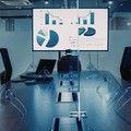 Modern conference room with glass table and wall-mounted charts on a large display