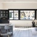 Modern living room with black-framed windows, white table, gray chairs, and sunlit wood floor