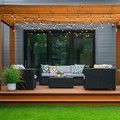 Covered backyard deck with wicker seating, string lights, and potted greenery
