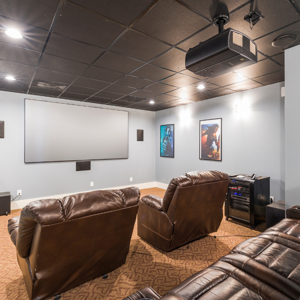 Home theater room with brown recliners, a large projection screen, and movie posters on white walls