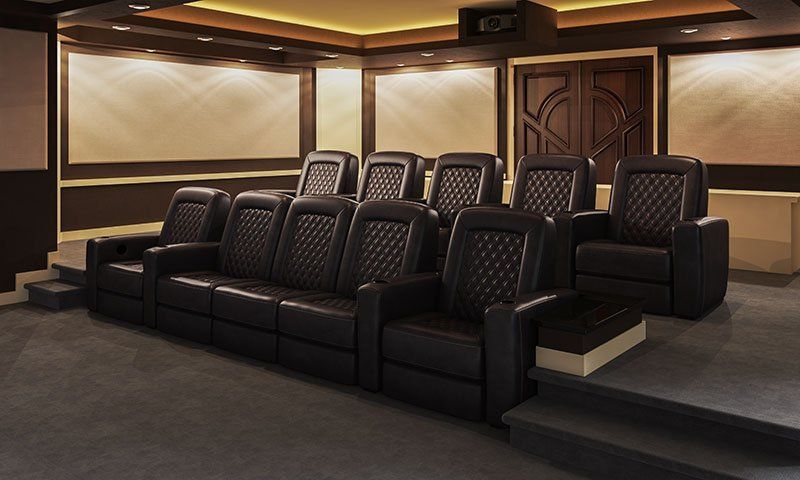 Luxury home theater with rows of black recliners and a large screen at the front