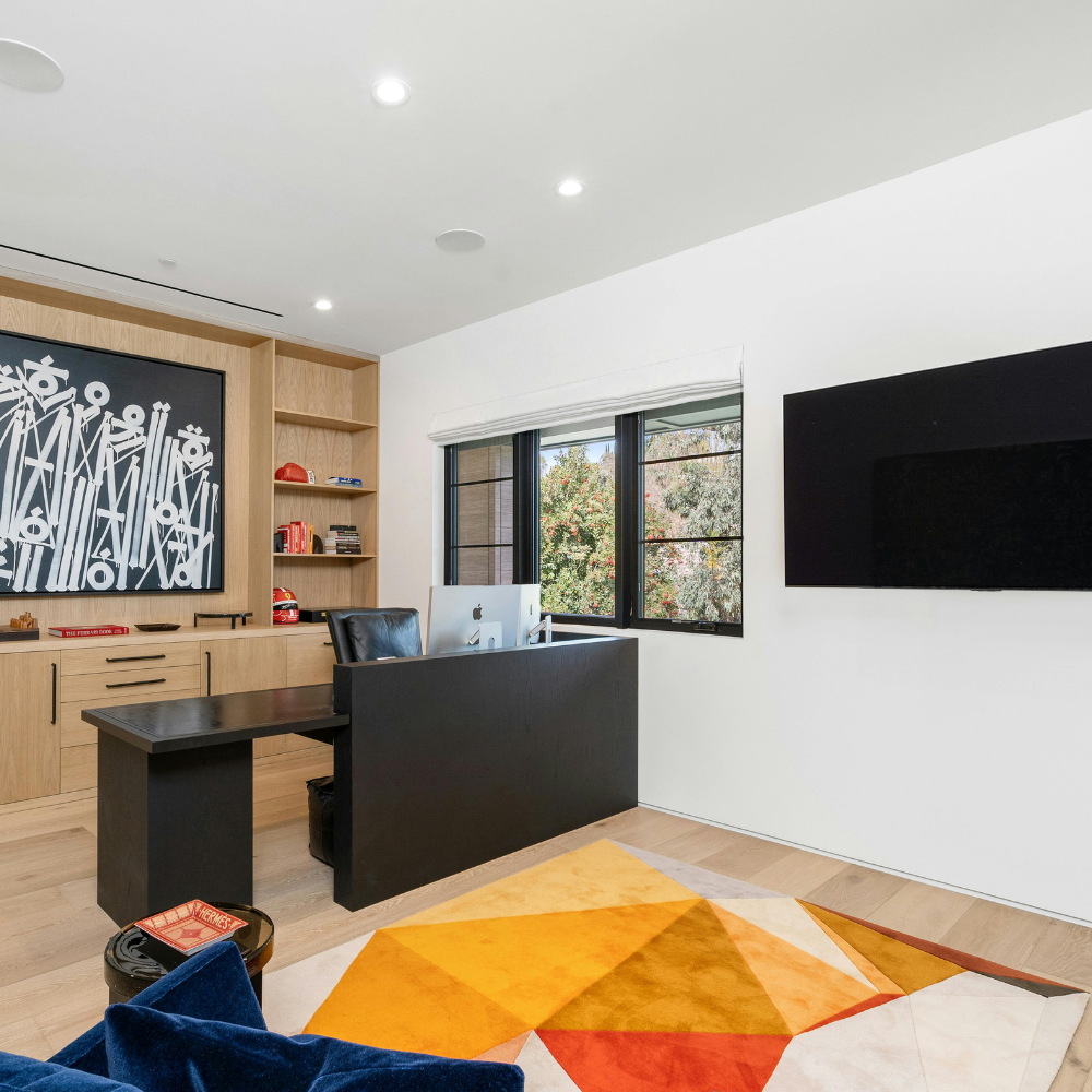Modern office with black desk, wall-mounted TV, bookshelf, and orange geometric rug