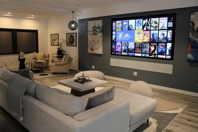 Modern living room with gray sectional, wall-mounted TV, dining area, and neutral decor