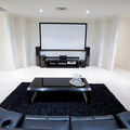 Modern home theater with projector screen, black rug, low coffee table, and leather sofa in a bright room