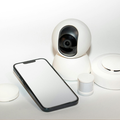 White security camera beside a smartphone and smart home devices on a white surface