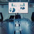 Modern conference room with glass table and wall-mounted charts on a large display