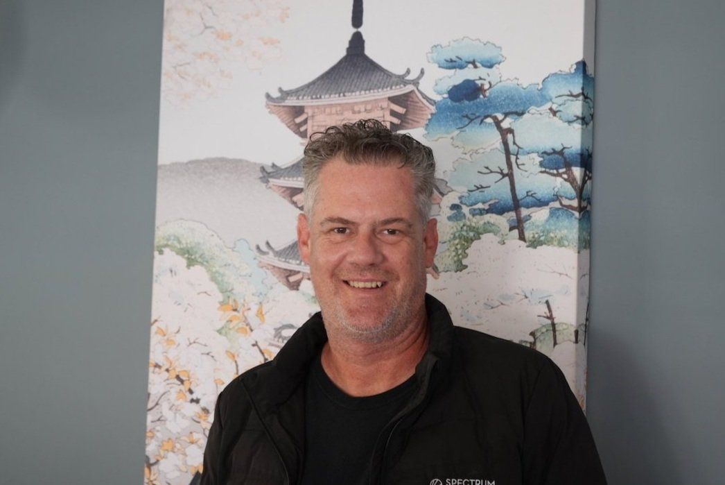 Smiling man in a black jacket standing indoors before a colorful wall mural