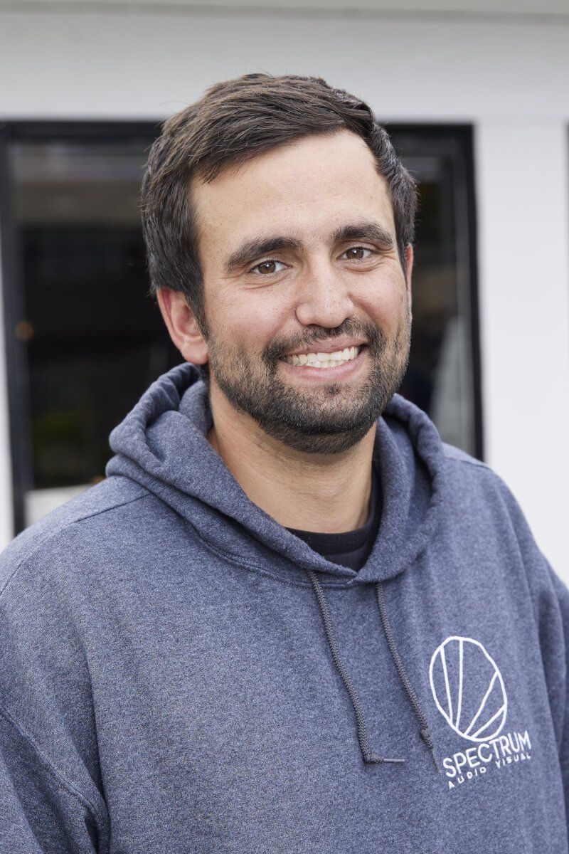 Smiling man in a blue hoodie standing outdoors in front of a building