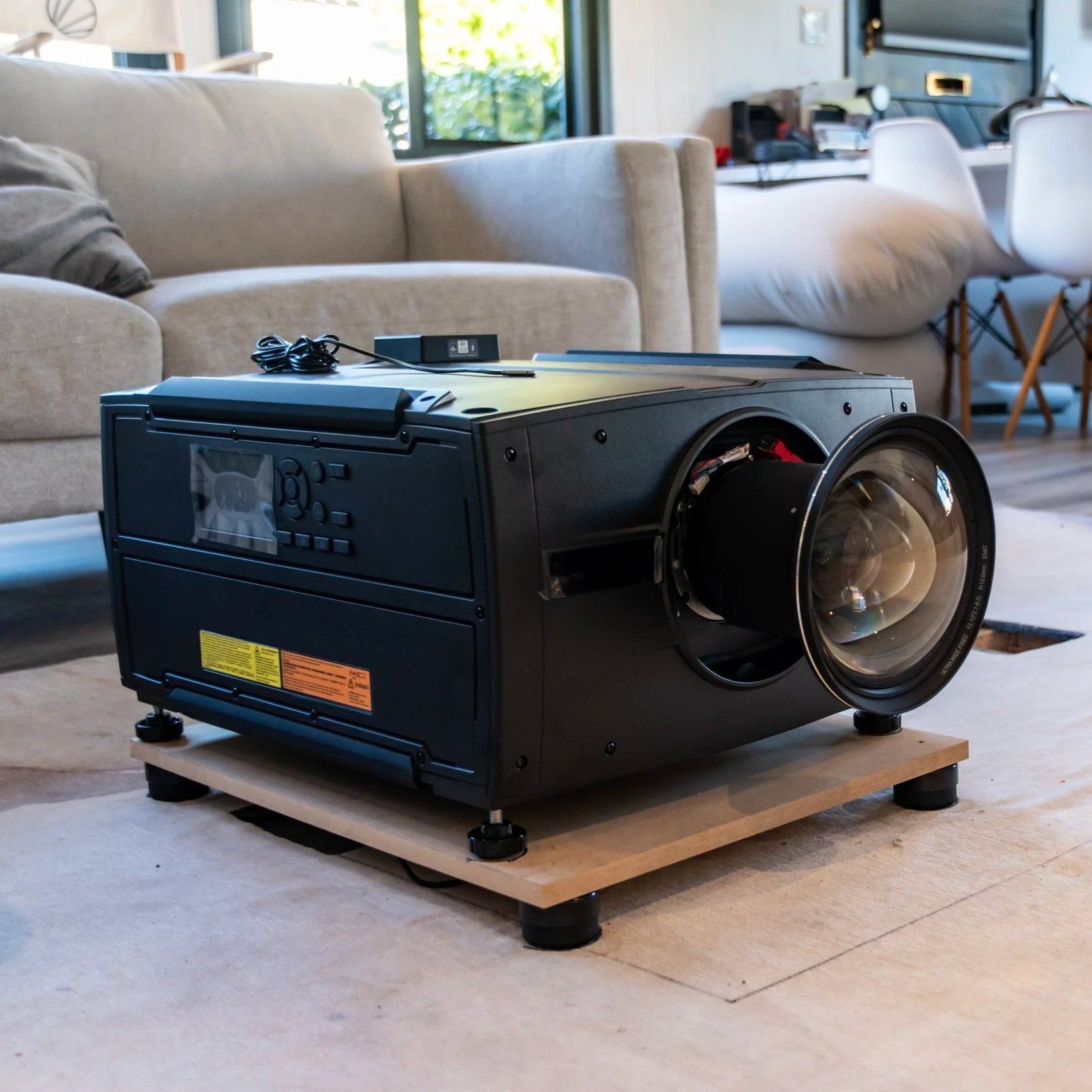 Black projector on a wooden platform in a living room with a couch in the background