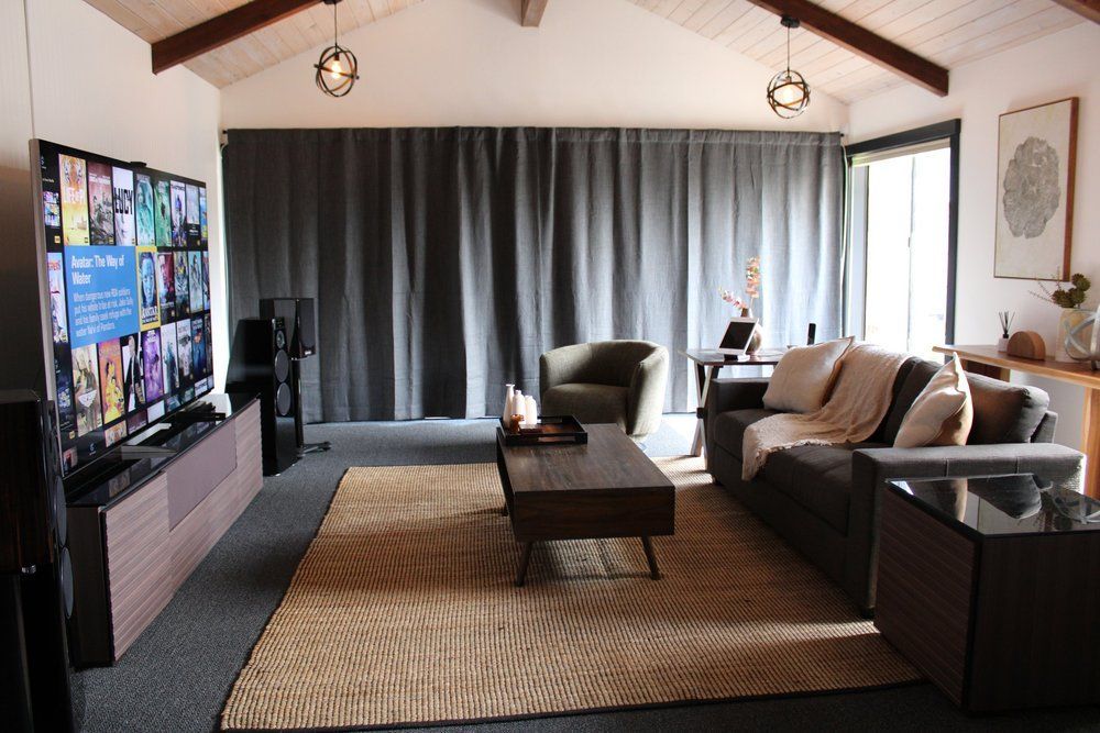 Modern living room with sectional sofa, coffee table, TV, curtains, and recessed ceiling beams