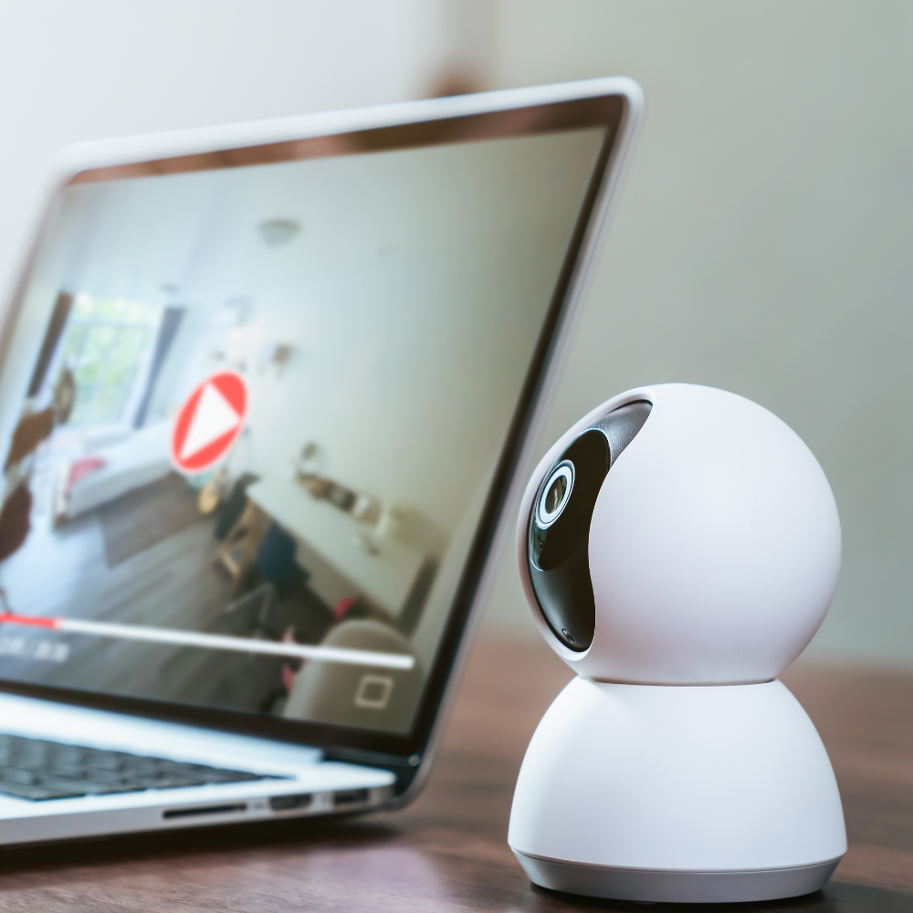 White home security camera beside a laptop playing a video on screen