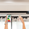 Hands holding a phone and AC remote near a wall-mounted air conditioner with an energy rating label
