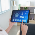 Person using a tablet to control a smart home dashboard showing temperature and settings in a bright living room