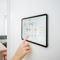 Hand pointing at a wall-mounted smart home control tablet with icons on a white wall