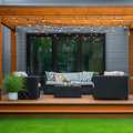 Modern backyard patio with wicker seating, string lights, and a wooden pergola in front of a house