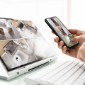 Hands using a smartphone to view a laptop screen showing a home interior security camera feed