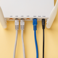 Back of a Wi‑Fi router with labeled ports and cables plugged in, including white, blue, and black cords.