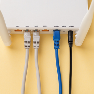 Back of a Wi‑Fi router with labeled ports and cables plugged in, including white, blue, and black cords.