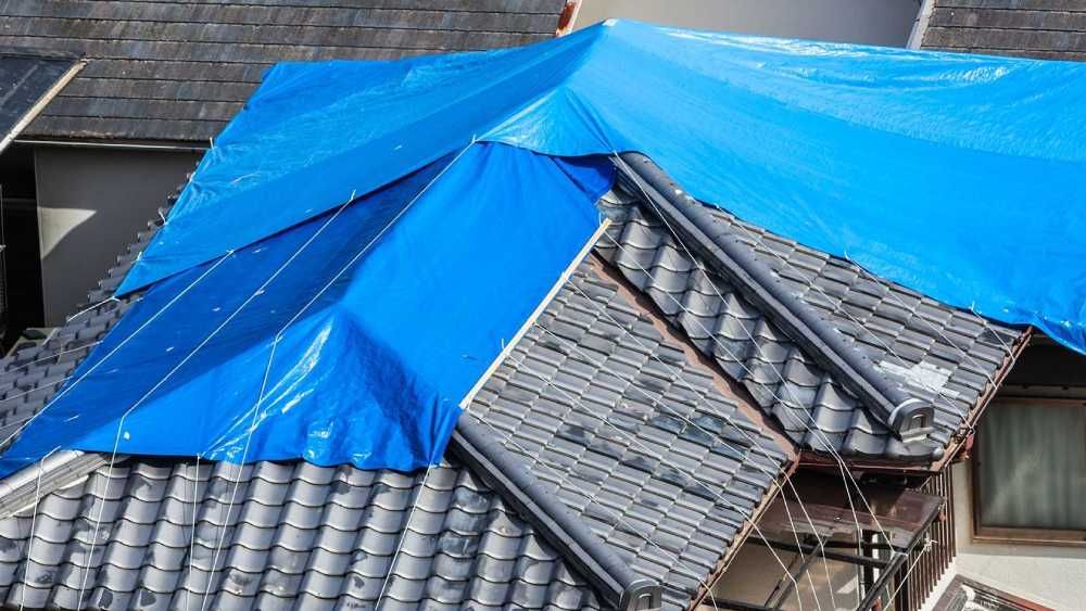 A blue tarp is secured over a section of a tiled roof to provide temporary protection  in Huntsville AL by LJ Roofing