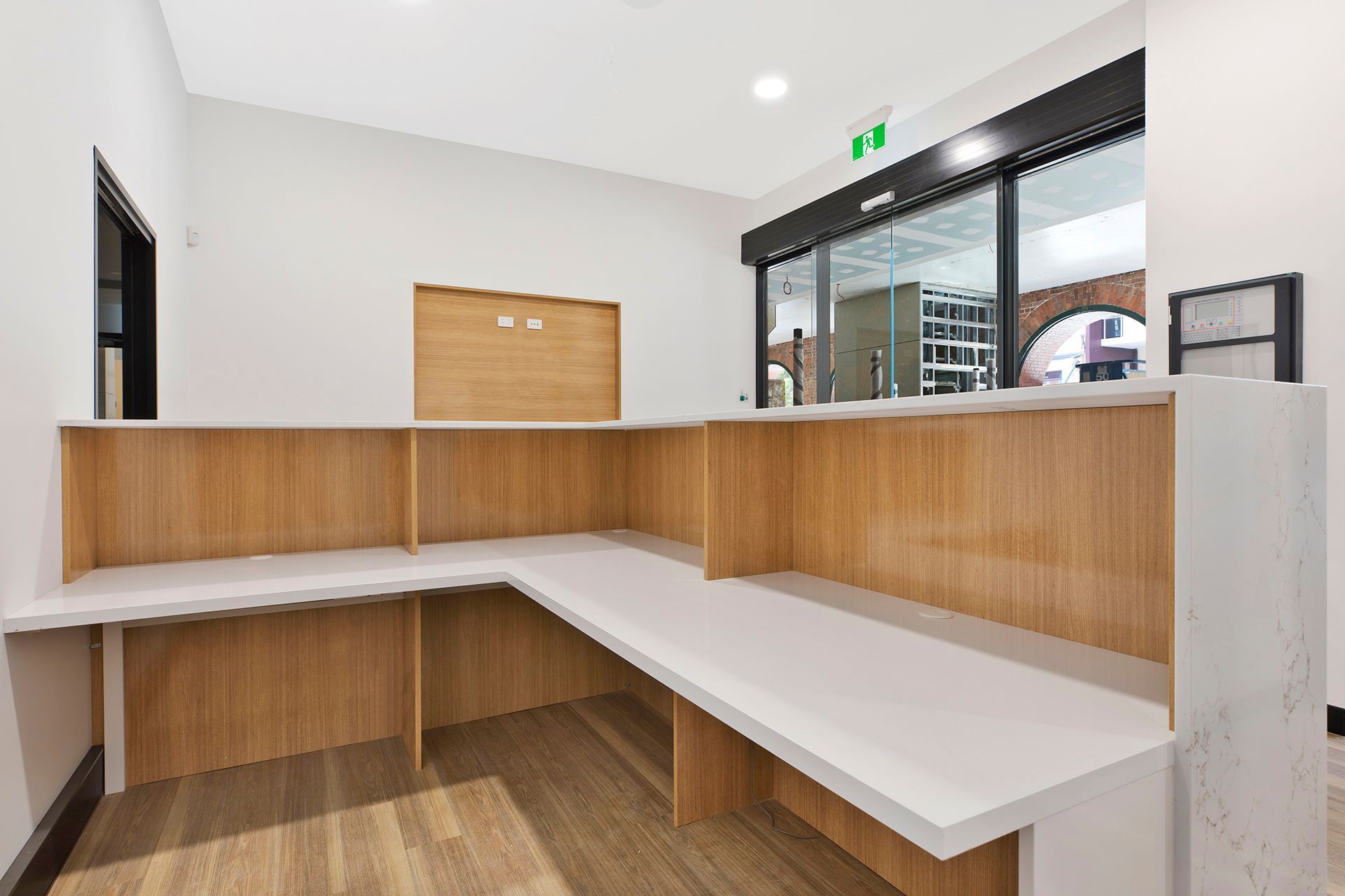 An empty L-shaped reception desk with wood paneling and white countertops in a bright, modern office space. — Trim Joinery In Fountaindale, NSW