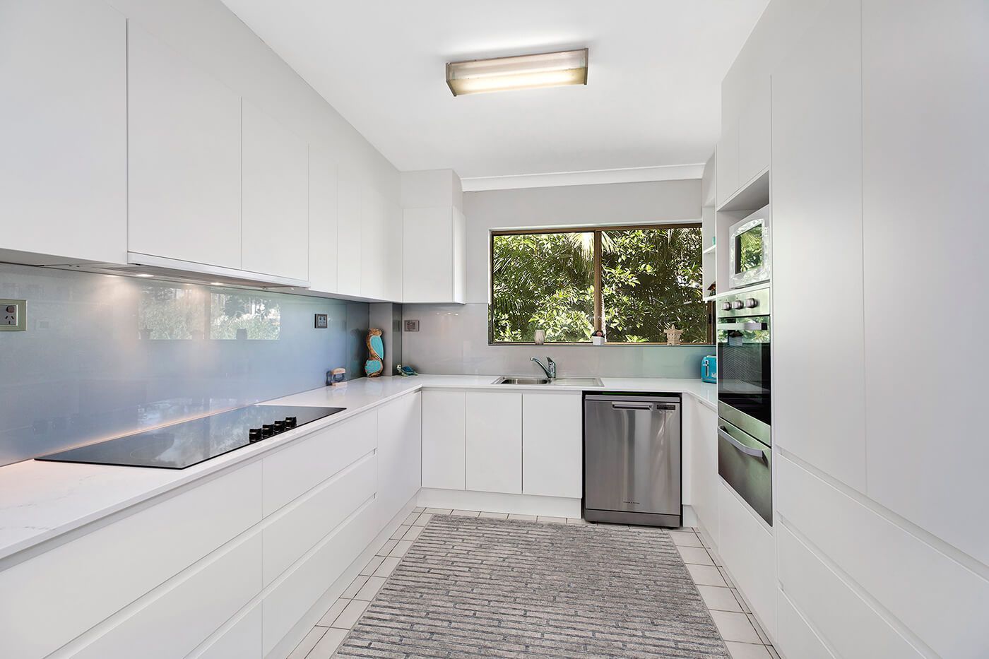 White Galley Kitchen With Cabinets, Appliances, and a Window — Trim Joinery In Fountaindale, NSW