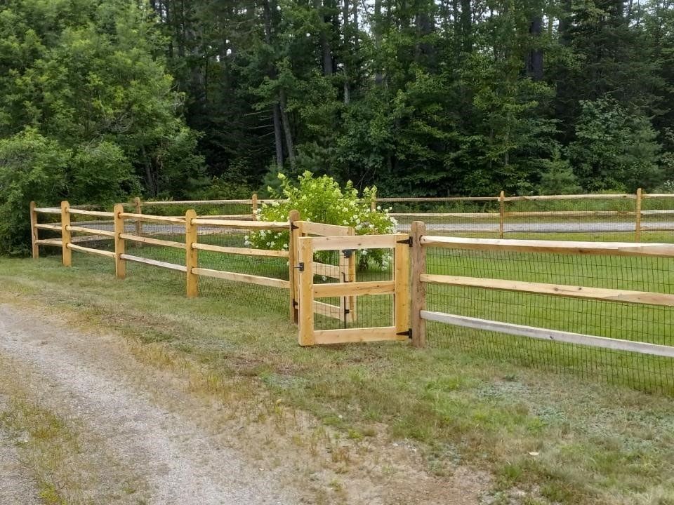 a wooden fence with a gate in the middle of a grassy field .