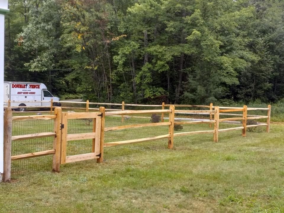 a wooden fence with a gate in the middle of a grassy field .