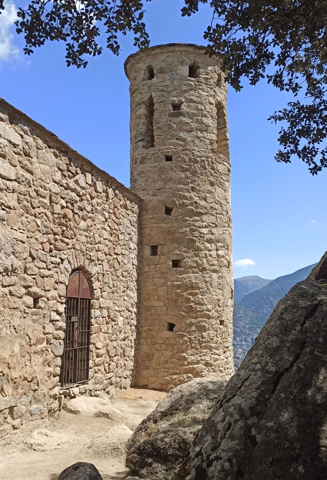 Torre de pedra al costat d'una paret rústica en un pati de muntanya sota un cel blau