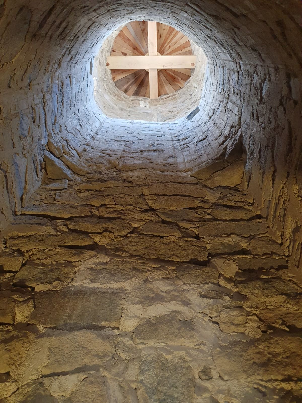 Mirant cap amunt d'un eix de pedra cap a una coberta rodona de fusta amb un patró creuat a sobre