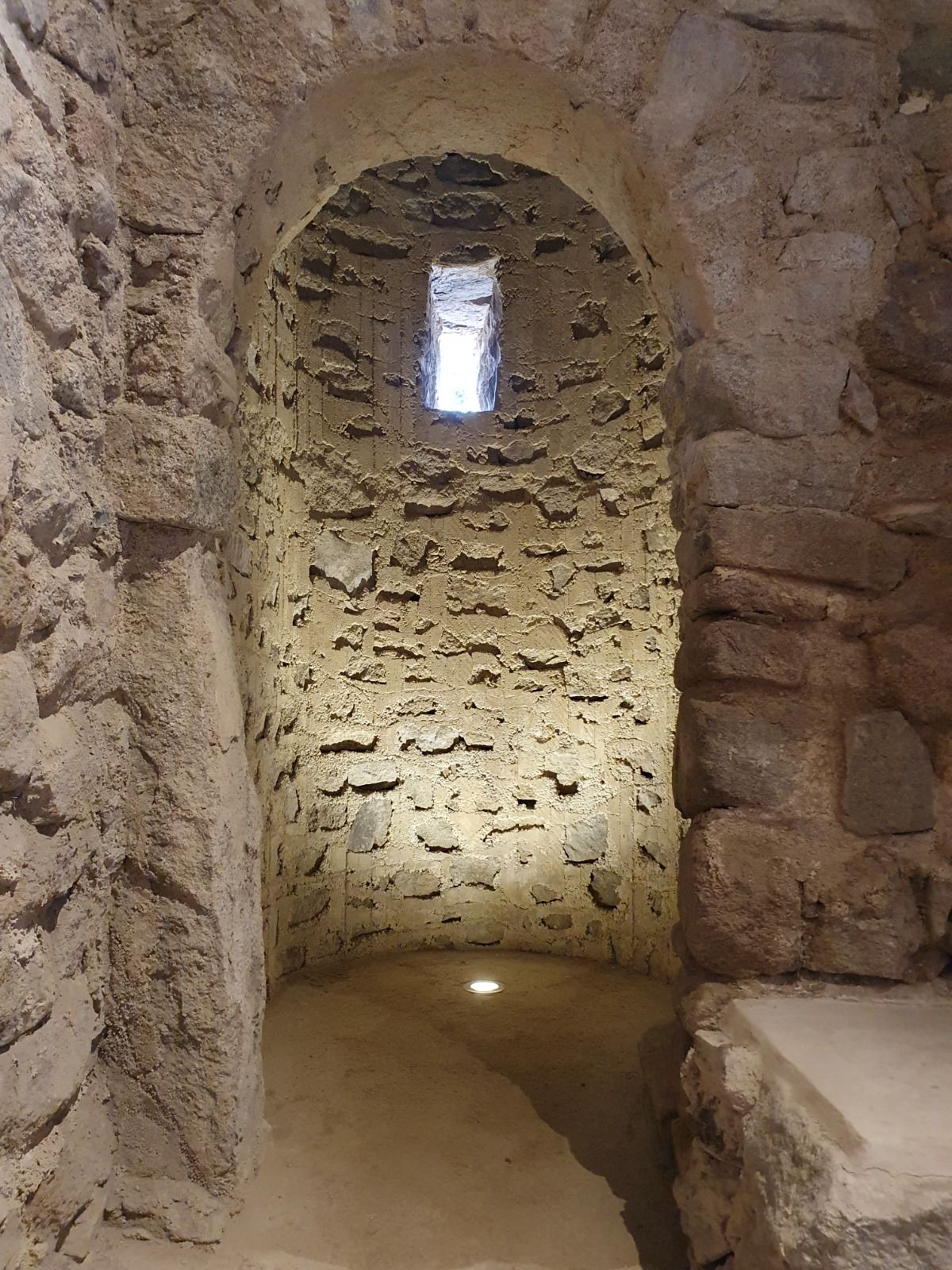Passadís de pedra en una antiga ruïna, amb una porta d'arc i una petita finestra a sobre.