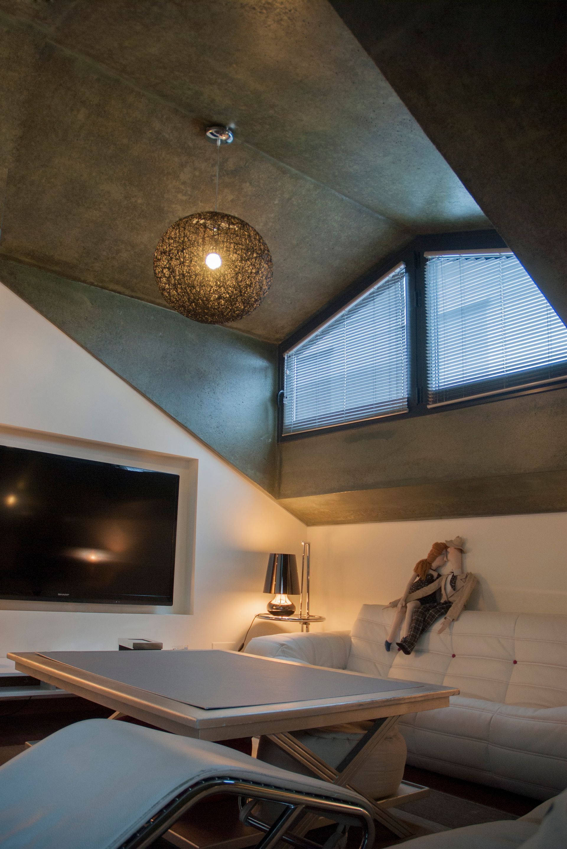 Sala d'estar moderna amb sofà seccional, taula baixa, televisor de paret i sostre inclinat amb finestres altes i llum penjant