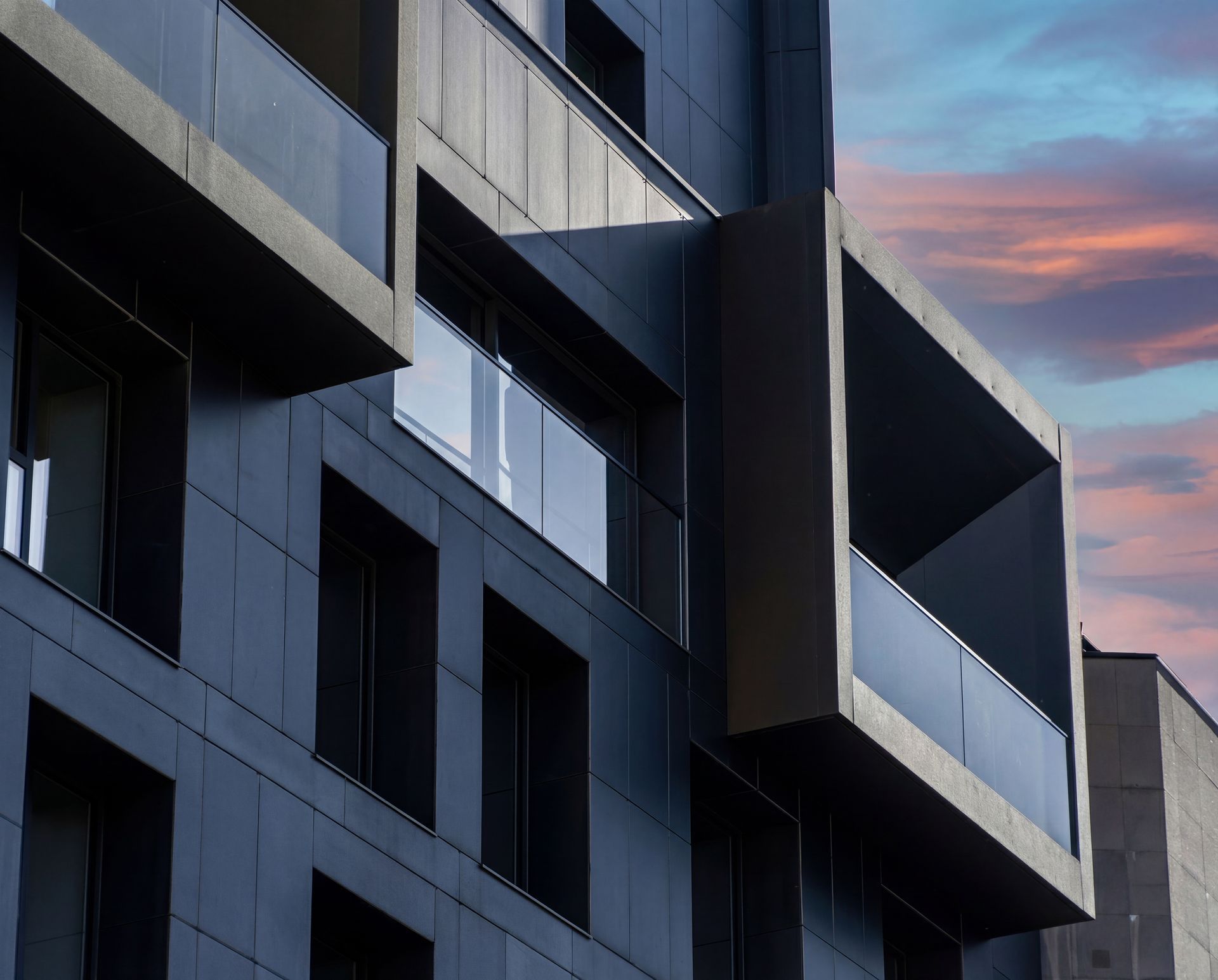 Edifici d'apartaments modern i fosc amb balcons geomètrics contra un cel rosat de posta de sol
