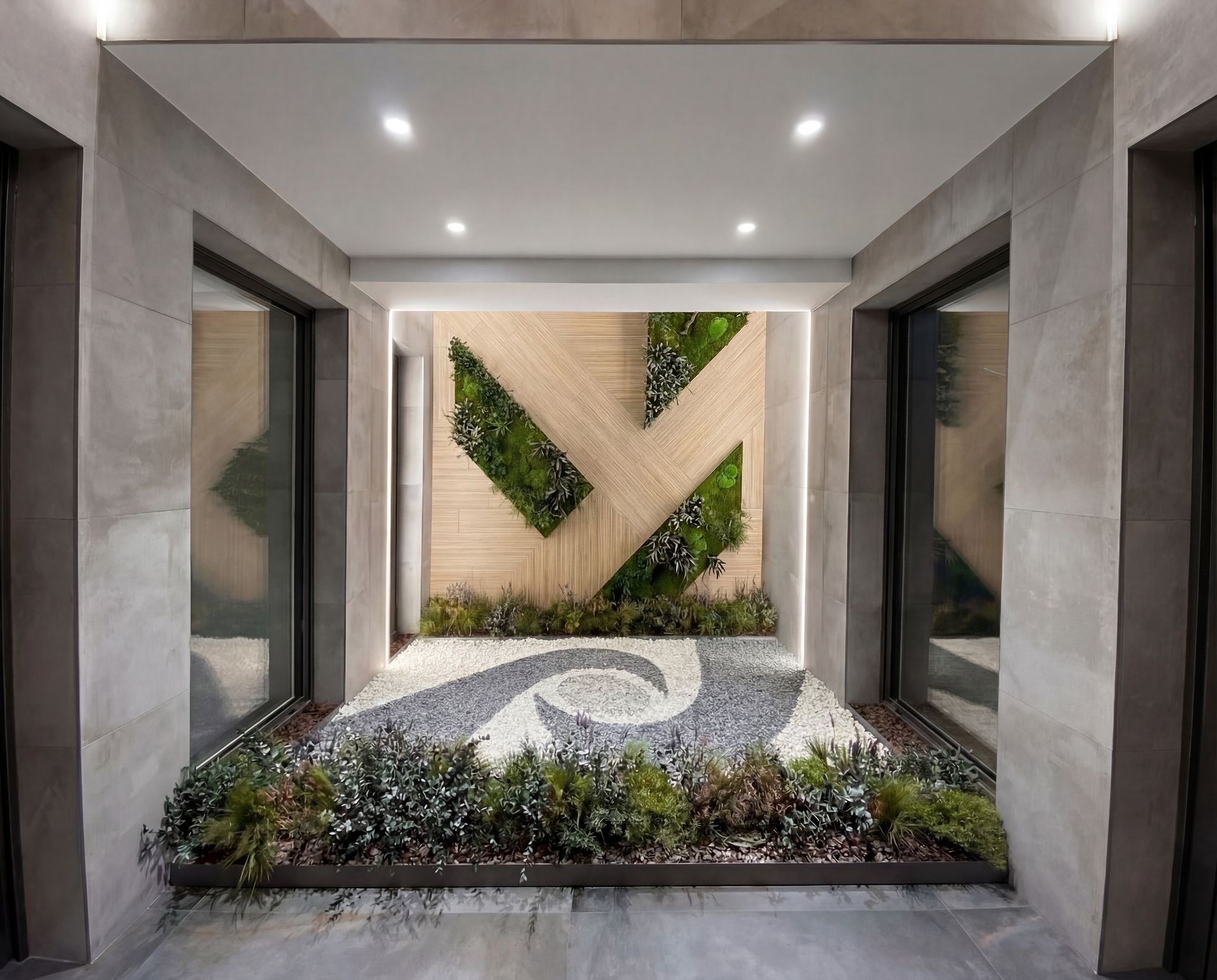 Entrada moderna amb parets beix, art mural geomètric amb vegetació i una jardinera sota llums encastades.