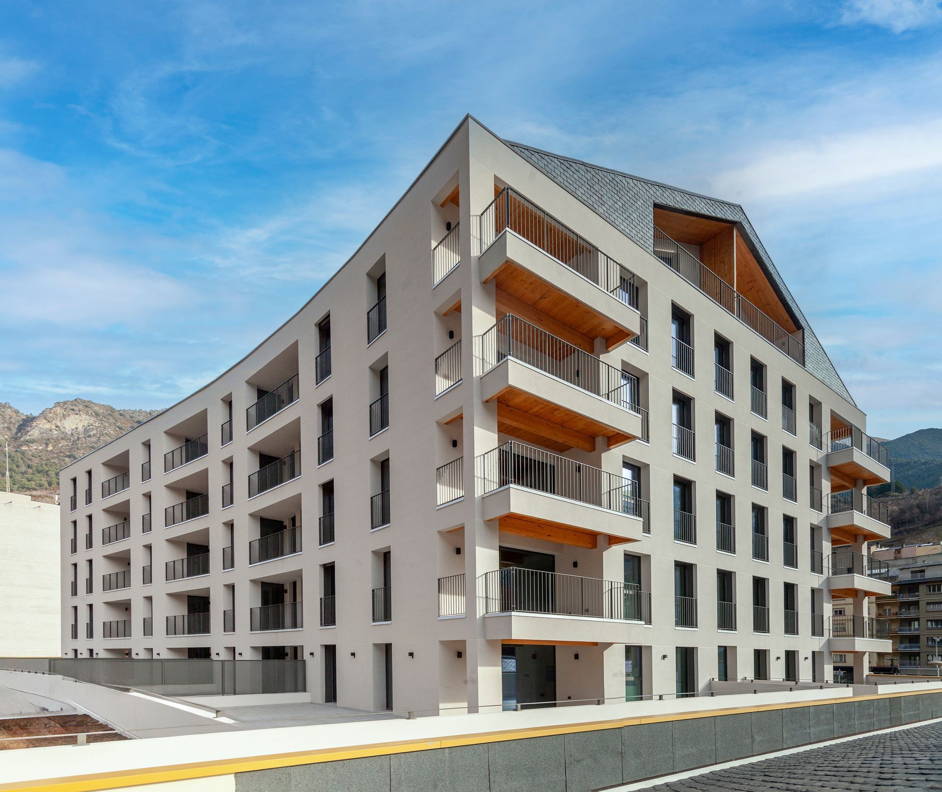 Edifici d'apartaments modern amb balcons i teulada inclinada en un carrer sota un cel blau