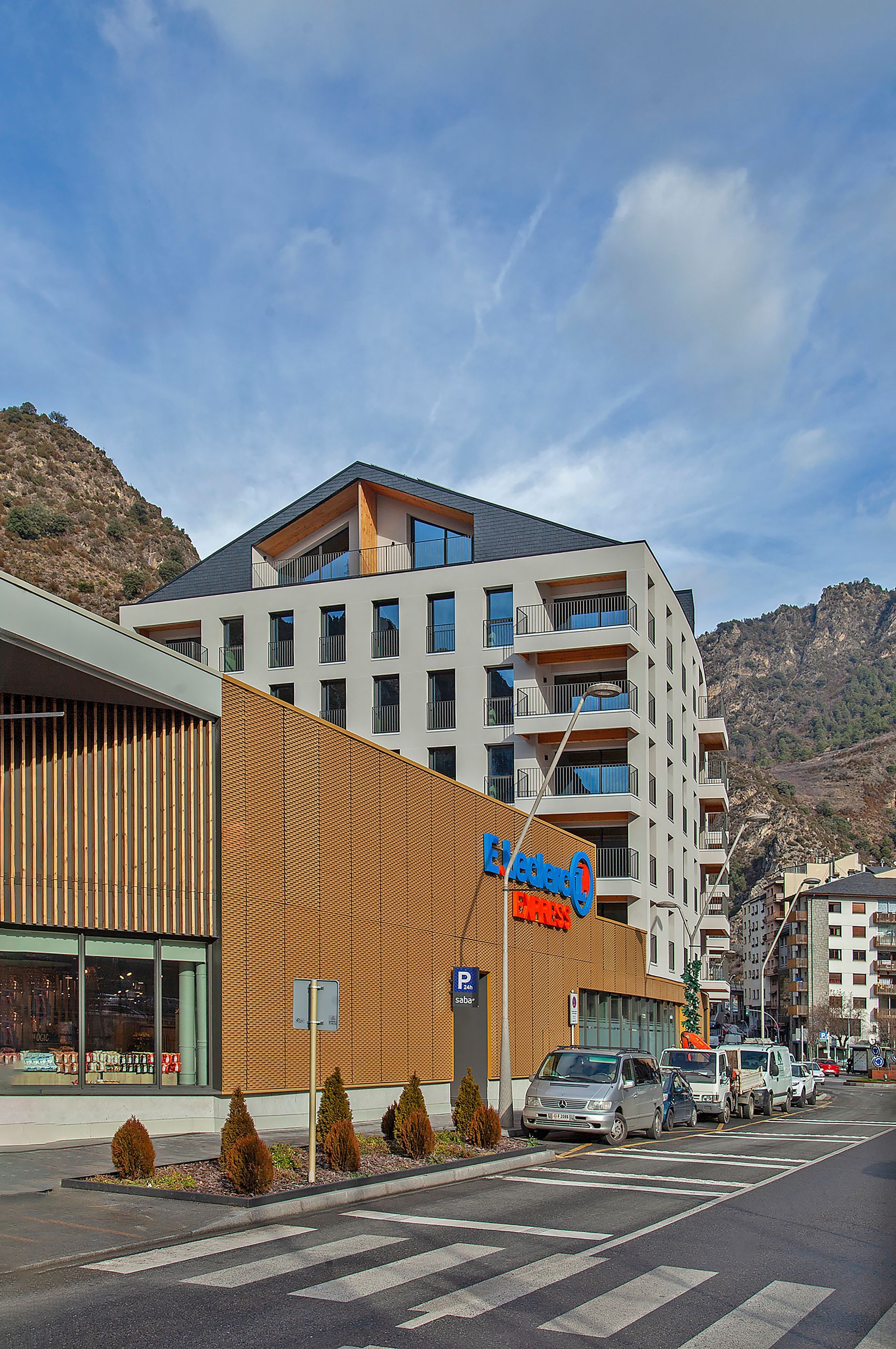 Hotel blanc modern al costat d'un edifici ondulat amb façana de fusta en un carrer de la ciutat amb muntanyes al fons
