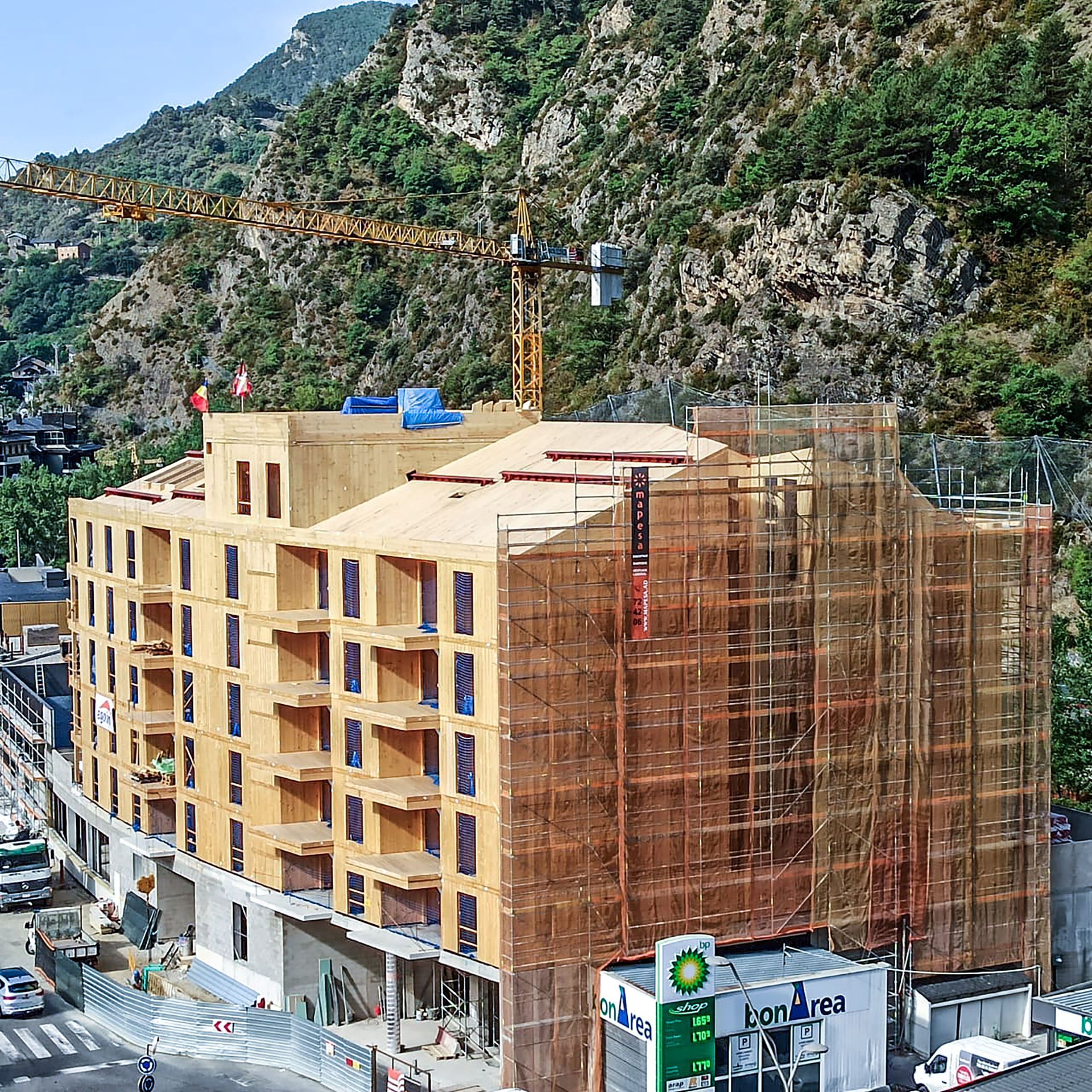 Edifici de diversos pisos en construcció amb bastides al costat d'un vessant rocós i grua.
