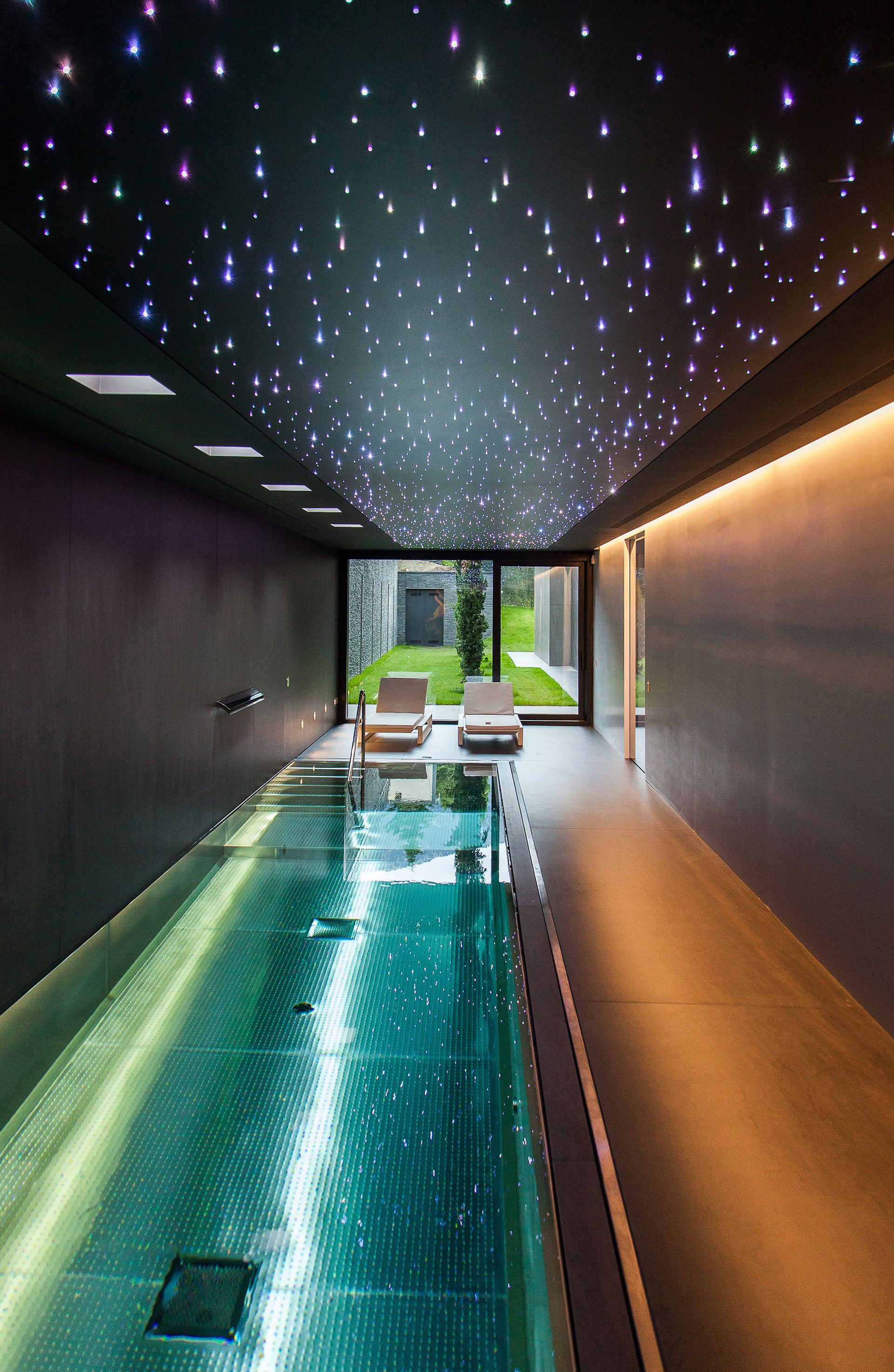 Piscina interior amb aigua turquesa, passarel·la estreta i llums de sostre estrellades que condueixen a una obertura lluminosa