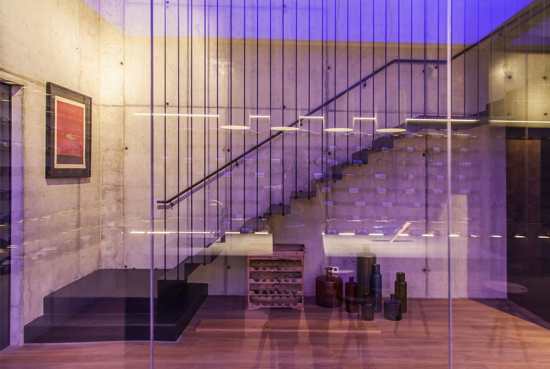 Escala moderna del vestíbul amb barana de vidre, il·luminació morada i una petita zona d'estar