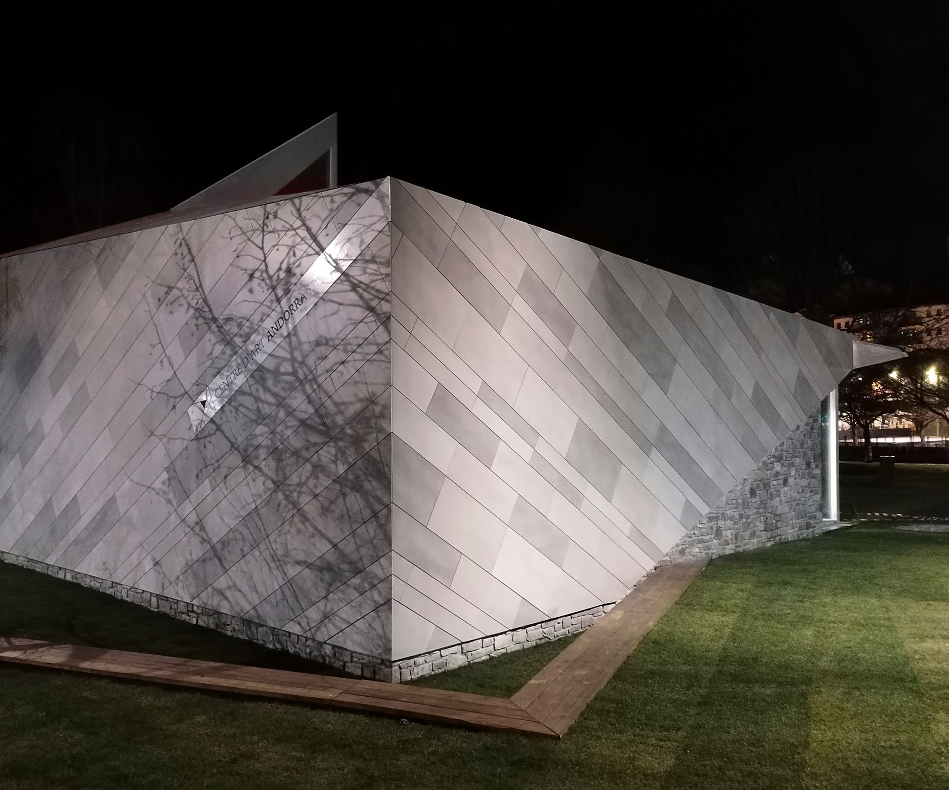 Escultura geomètrica de pedra blanca il·luminada a la nit sobre una gespa