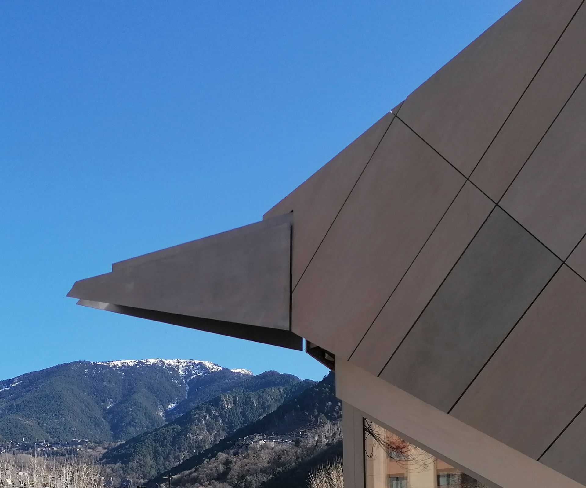 Façana d'edifici modern amb voladís angular contra el cel blau i les muntanyes nevades