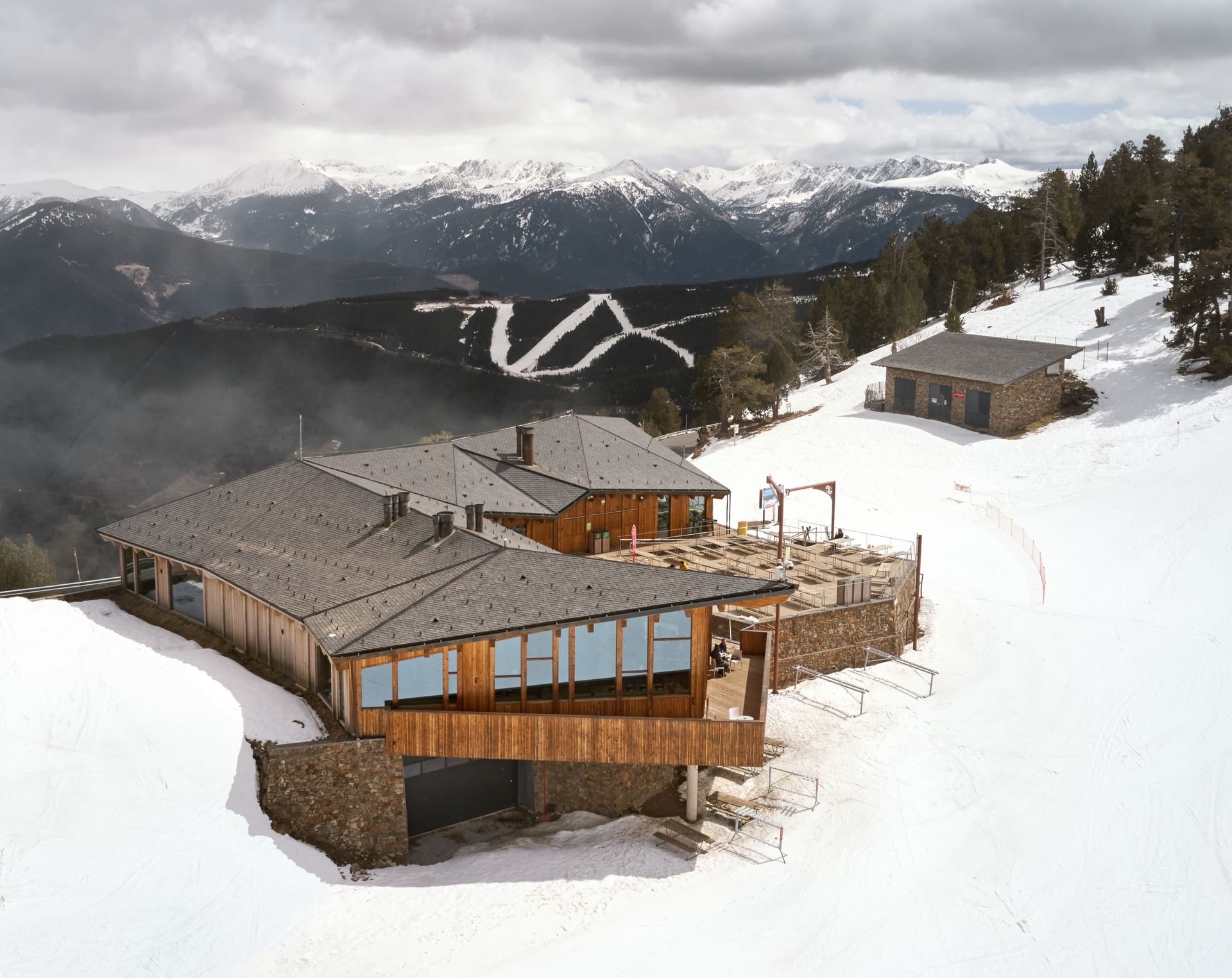 Complex de refugis de muntanya cobert de neu amb cabanes de fusta i pistes d'esquí al fons